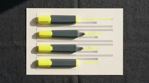 Four highlighter pens laid side by side on blank cards over a page, each with its own test stroke